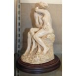 A resin sculpture of a couple embracing on wooden plinth.