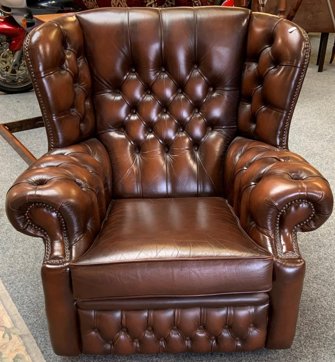 A brown leather button back wing armchair (matches lot 288).