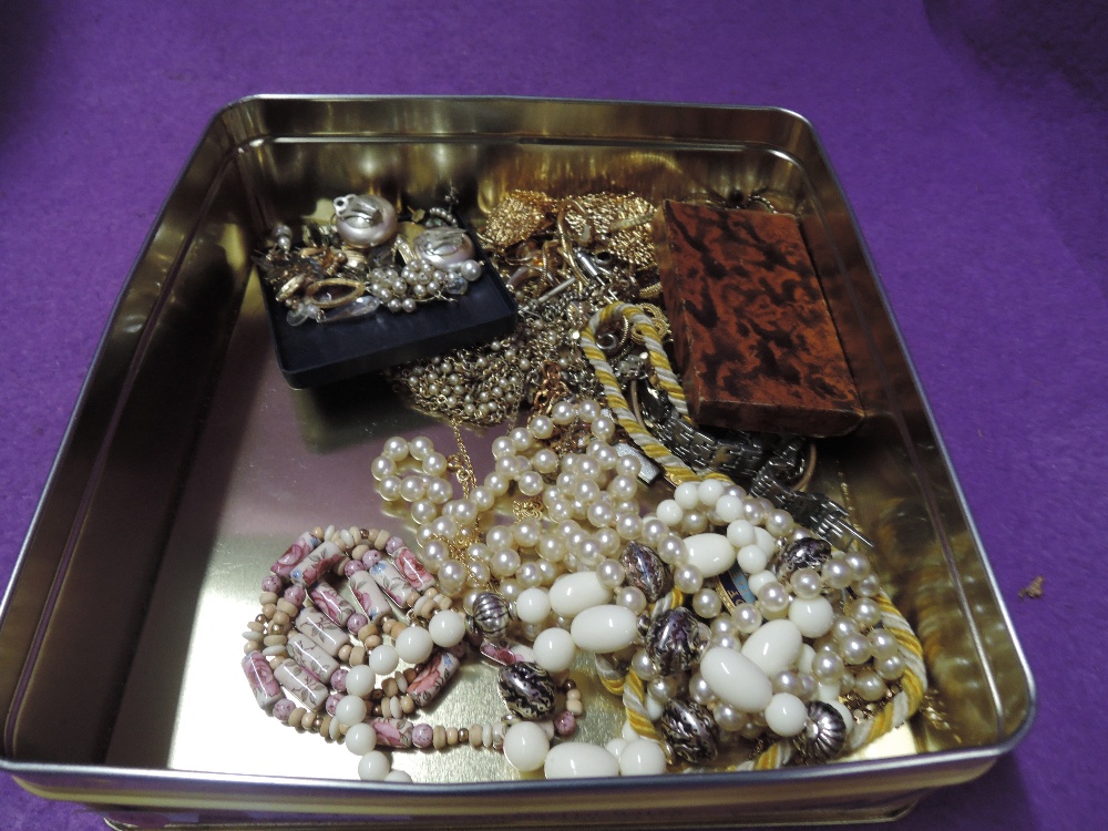 A tin of costume jewellery including strings of beads, chains, earrings etc