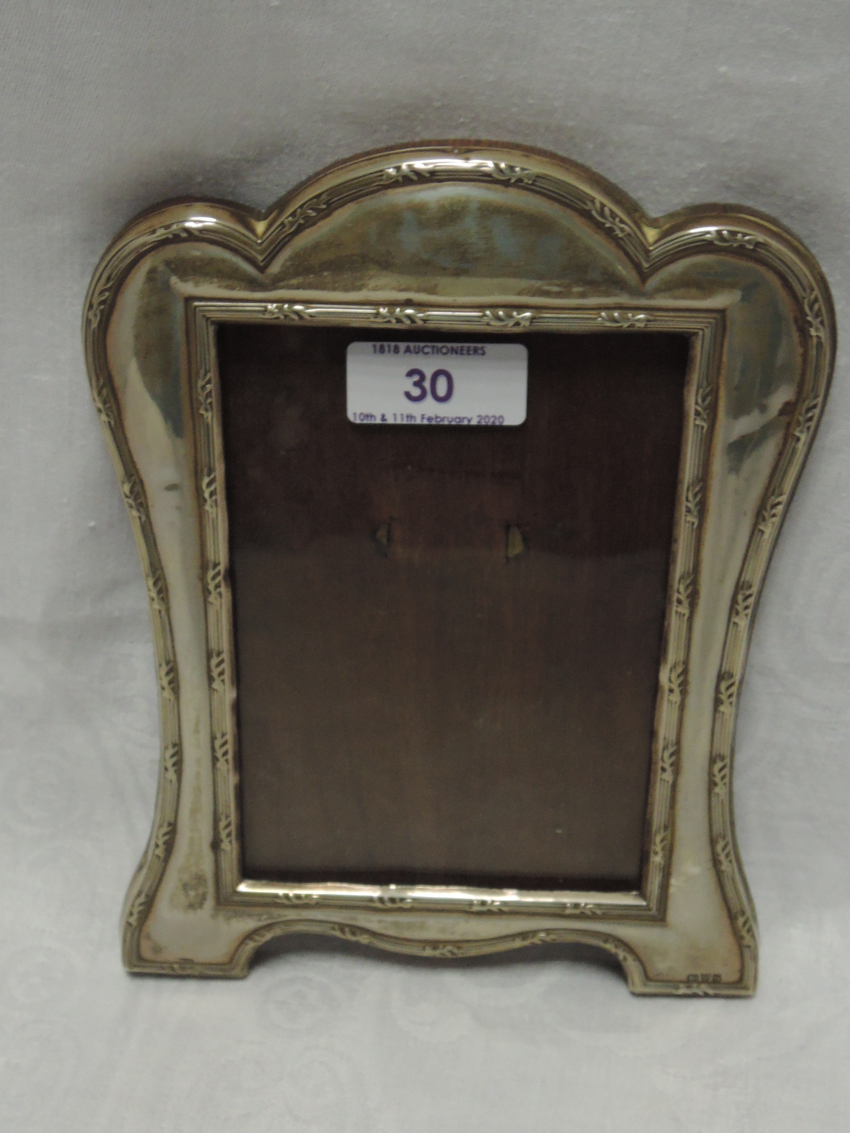 A silver photograph frame of shaped rectangular form having reed and leaf decoration and wooden