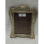 A silver photograph frame of shaped rectangular form having reed and leaf decoration and wooden