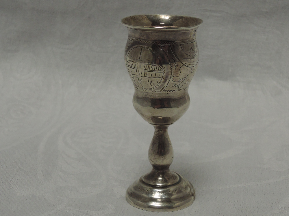 A small Russian silver vodka goblet having scenic engraving with baluster stem to stepped circular
