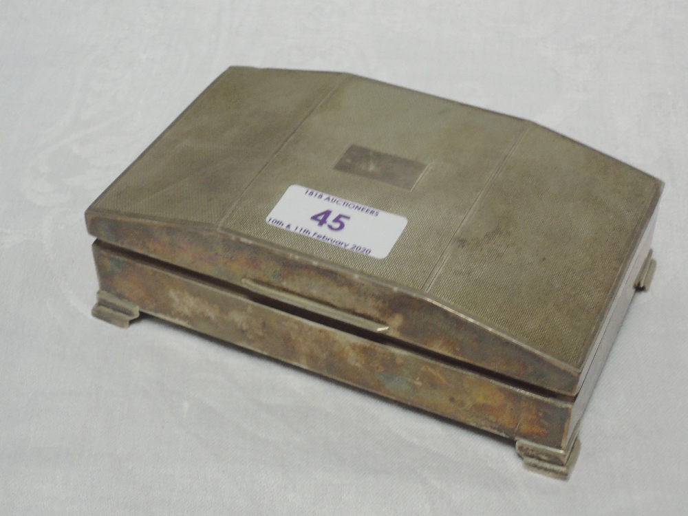 A silver cigarette box having bracket feet and engine turned decoration to raised lid, Birmingham