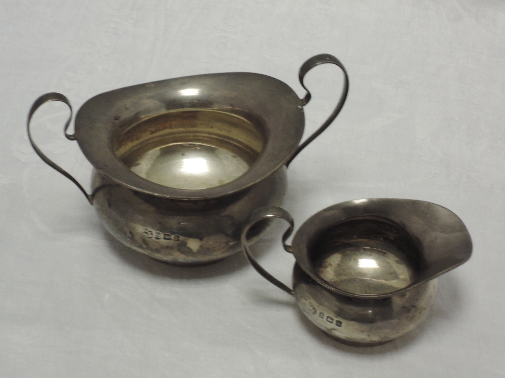 An Edwardian silver sugar bowl and cream jug of plain form having loop handles, Birmingham 1907,