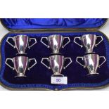 A cased set of six Edwardian silver tot glasses of two handled trophy form, London 1904, Wakeley &