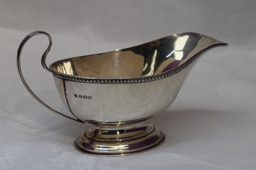 A silver sauce boat having gadrooned rim, loop handle and pedestal foot, Birmingham William