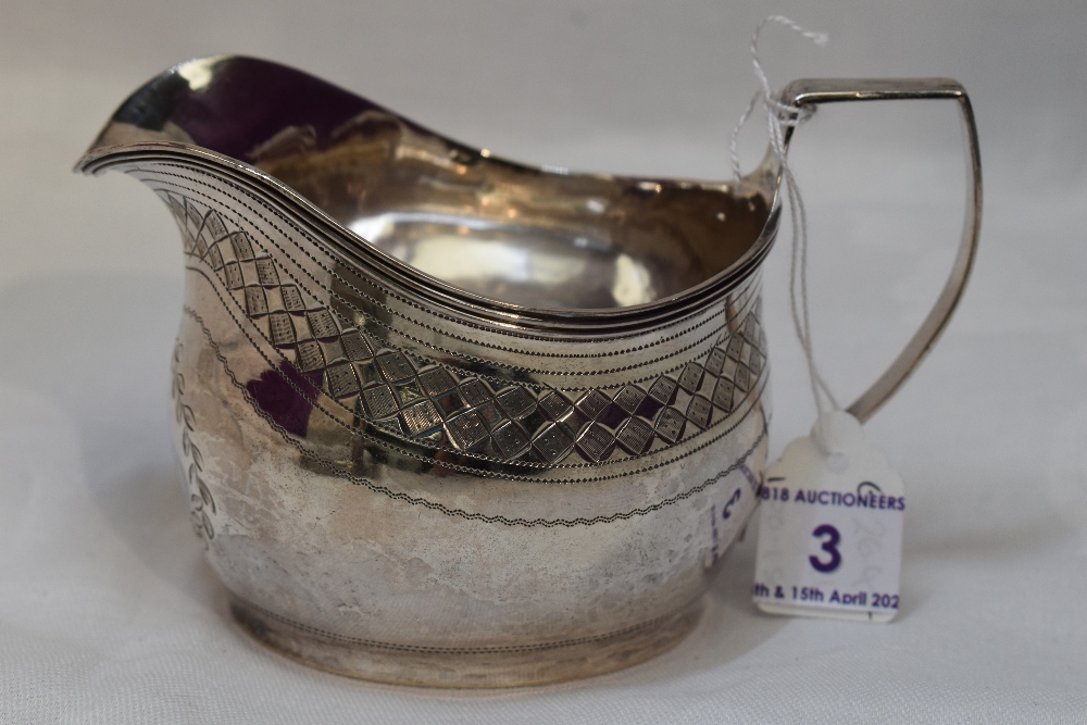 A Georgian silver cream jug of helmet form having bright cut decoration and monogram to cartouche,