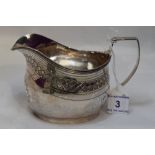 A Georgian silver cream jug of helmet form having bright cut decoration and monogram to cartouche,