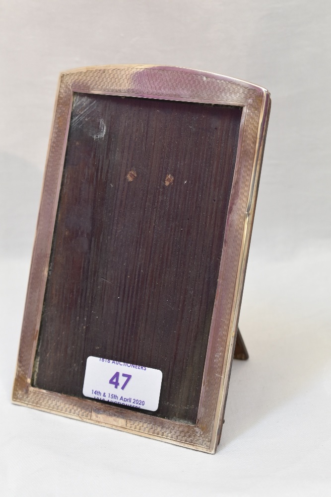 A silver photograph frame having arched top and engine turned decoration with wooden easel back