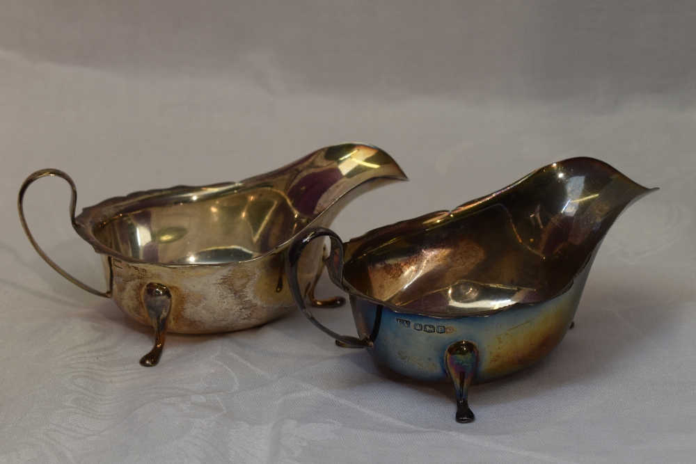 A pair of silver sauce boats of plain form having shaped rims, loop handles and trefoil paw feet,