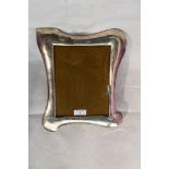 A large rectangular silver photograph frame of moulded curved form, having wooden easel stand to