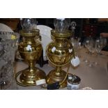 Two electric brass oil lamp style table lamps, both having glass chimneys.