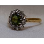 A lady's dress ring having a peridot style and diamond cluster in a stepped claw mount on an 18ct