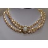 A triple string of cultured pearls of even form having a large oval yellow metal box clasp stamped