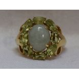 A lady's dress ring having an oval jade cabouchon within a peridot set border to shaped shoulders on