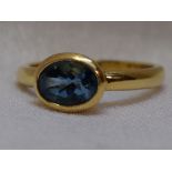 A ladies dress ring having an oval blue topaz in a collared mount on an 18ct gold loop, size M