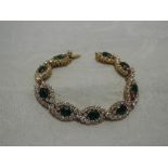 An emerald and diamond articulated bracelet having nine oval cut emeralds within a scrolling