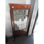 A 1920s mahogany display cabinet of narrow proportions having leaded glass panel door on splay legs.