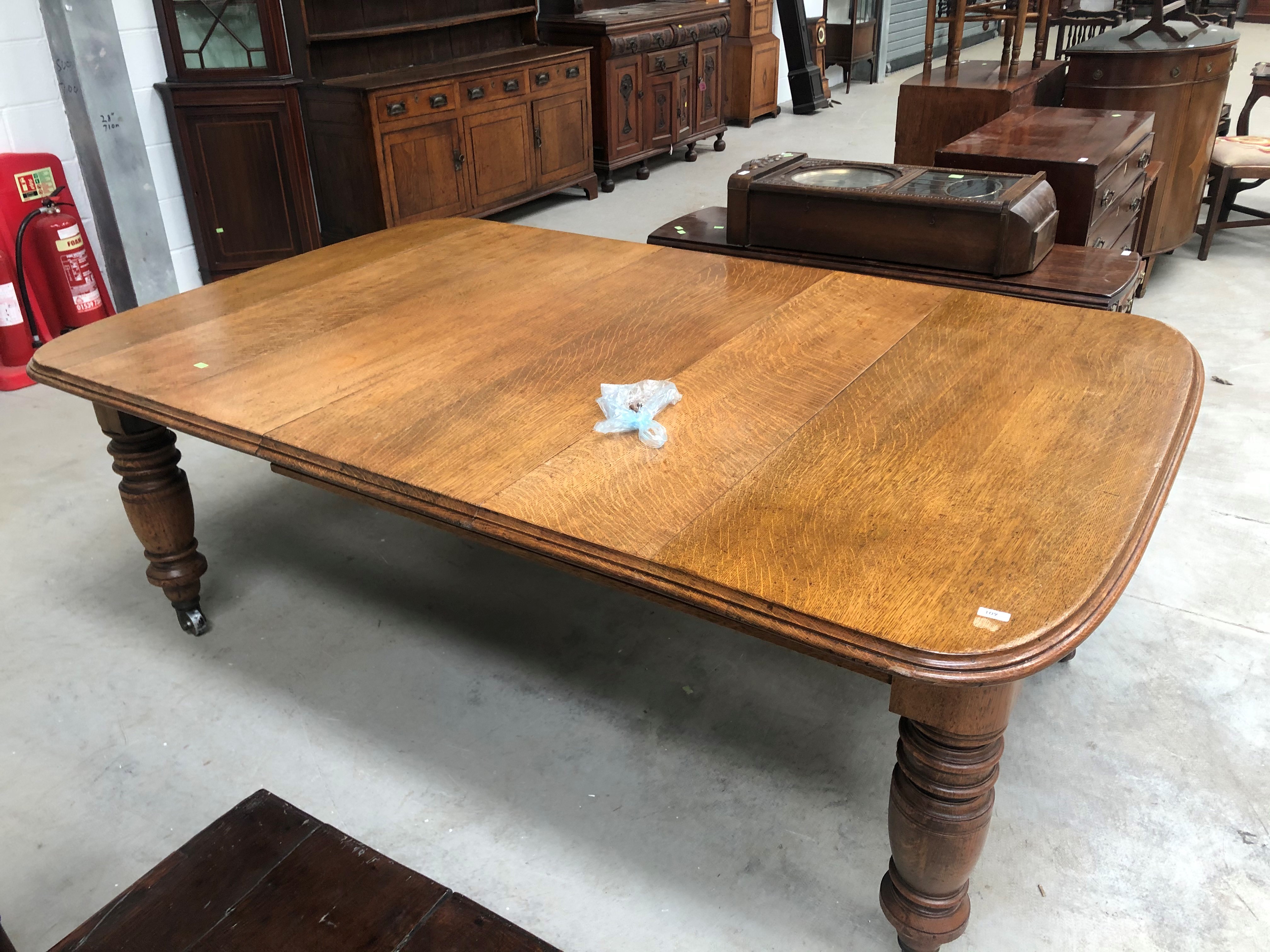 A late Victorian golden oak dining table on heavy turned legs with extra leaf, closed width approx