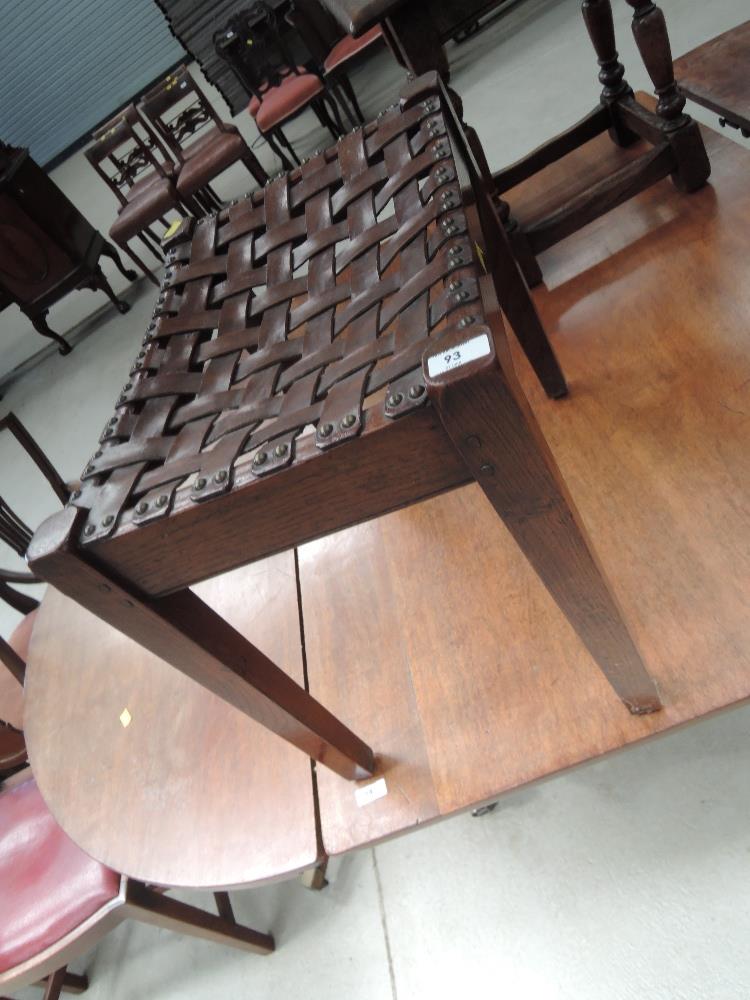 An early 20th Century oak stool in the Arts and Crafts Simpson style with leather strapwork top,