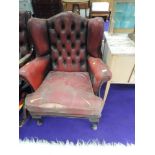 A vintage red leather wing back armchair, very grubby and worn