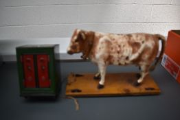 An early 20th century pull-along hide-covered papier mache cow on wood base with brass wheels,