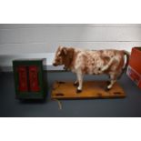 An early 20th century pull-along hide-covered papier mache cow on wood base with brass wheels,