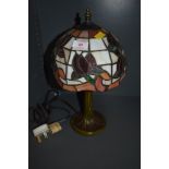 A stained glass table lamp having Tiffany style shade and metal base styled as a tree trunk.