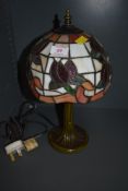 A stained glass table lamp having Tiffany style shade and metal base styled as a tree trunk.