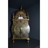 A brass cased lantern clock with chased floral face and a later electric movement