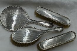 A silver part dressing table set having mirror and three brushes, all with engine turned striped