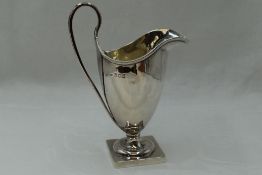 An Edwardian silver cream jug of plain helmet form having reided loop handle and square platform