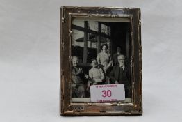 A small silver photograph frame of rectangular form having decorative border and wooden easel