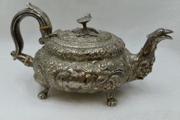 A Georgian silver teapot of squat form having a floral finial, heavily embossed floral decoration,