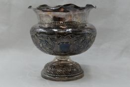 A white metal pedestal bowl having frilled edge, repousse scroll decoration to bowl and presentation