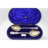 A cased pair of Edwardian silver fruit serving spoons having decorative scrolled rims and gilt