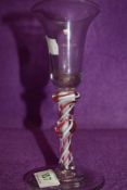 A wine glass having trumpet bowl on stem with a red ribbon twist surrounding a five strand opaque