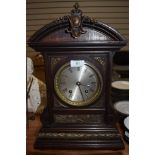 An ornate oak cased mantel clock with bevelled glass face and intricate metal decorations