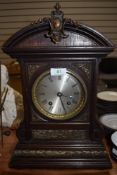 An ornate oak cased mantel clock with bevelled glass face and intricate metal decorations