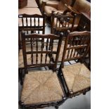 A set of four traditional oak spindle back dining chairs, having rush seats and turned frames (