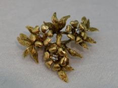 An 18ct gold brooch modelled as a stem of three flowers with diamond centres