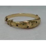 A 9ct gold hinged bangle having diamond and emerald chip decoration in star burst settings on