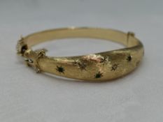 A 9ct gold hinged bangle having diamond and emerald chip decoration in star burst settings on