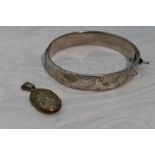 A HM silver hinged bangle having engraved scroll decoration and a small white metal oval locket