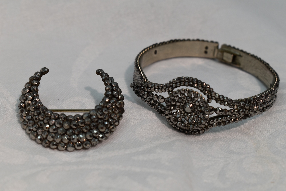 A cut steel tension bangle having pierced lozenge shaped panel and concealed clasp and a similar cut