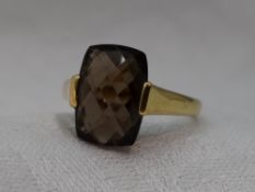 A lady's dress ring having a smoky quartz facetted panel in a tension mount on a 9ct gold loop, size