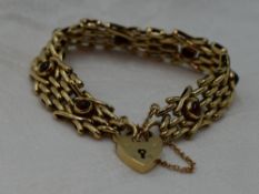 A 9ct gold fancy link gate bracelet having seven garnet set panels and a padlock clasp