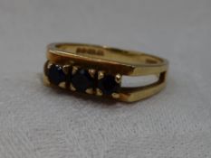 A lady's dress ring having a trio of sapphires in claw set mount to open shoulders on a 9ct gold
