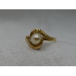 A lady's dress ring having a central cultured pearl in a stylised wave cross over mount to yellow