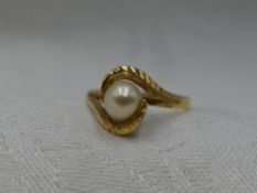 A lady's dress ring having a central cultured pearl in a stylised wave cross over mount to yellow